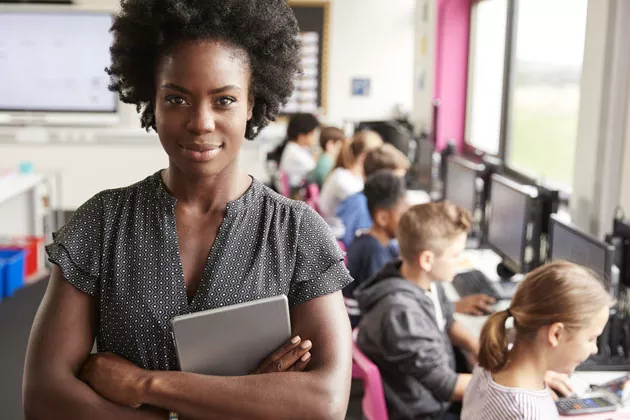 professora posando para foto enquanto os alunos estudam no computador
