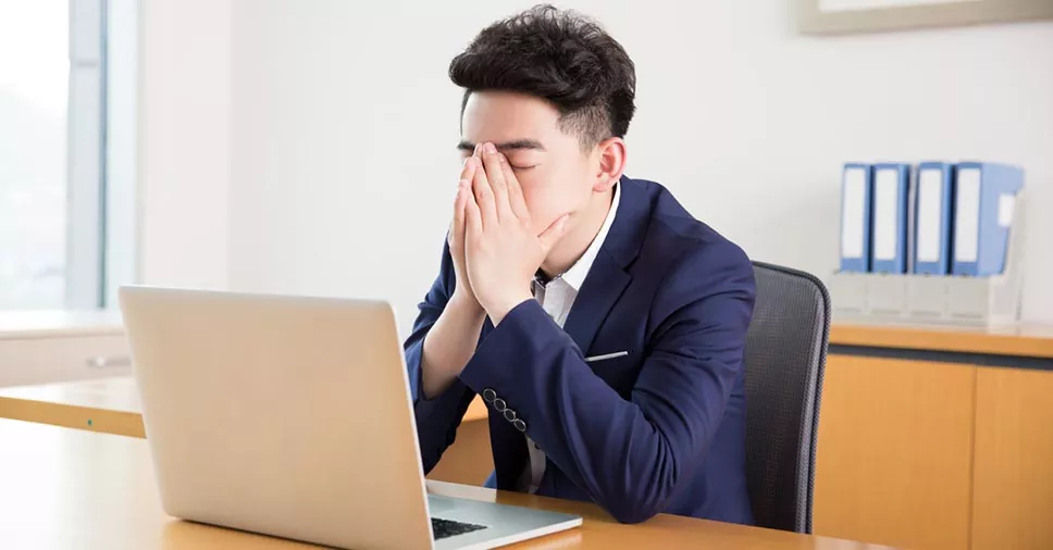 Homem de terno com as mãos no rosto olhando para o notebook